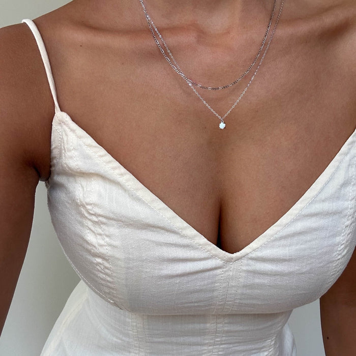 A woman wears a cream spaghetti strap dress with layered silver jewelry from LLUME Jewelry’s Daily Set Silver. The photo is cropped to show her chest and shoulders.