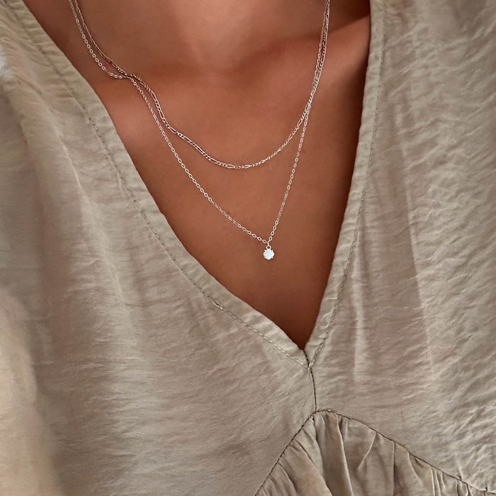 A person wearing a light beige V-neck blouse and LLUME Jewelry's Daily Set Silver—two delicate silver pieces—set against a neutral background.