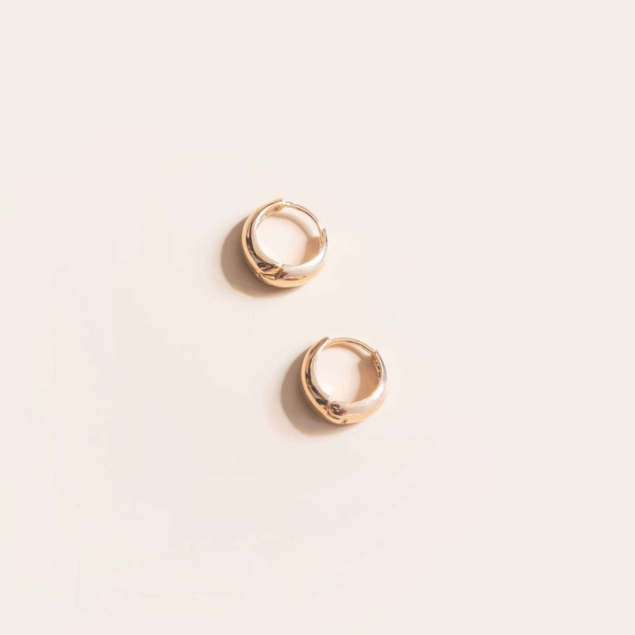 Two small Day-to-Day Hoop earrings by LLUME Jewelry, crafted in 18k gold, rest parallel on a light beige background—an elegant vintage-inspired touch for any jewelry collection.