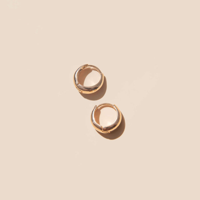 Two small, vintage-inspired Day-to-Day Hoop earrings by LLUME Jewelry gleam on a plain, light beige background with soft shadows.