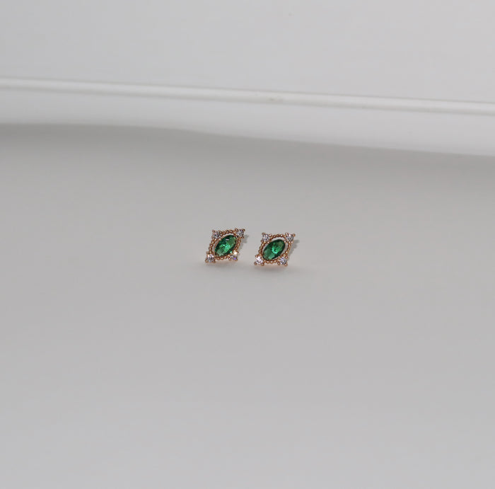 LLUME Jewelry’s Destiny Earrings in gold feature emerald green studs encircled by small clear stones, shown on a plain light gray background.