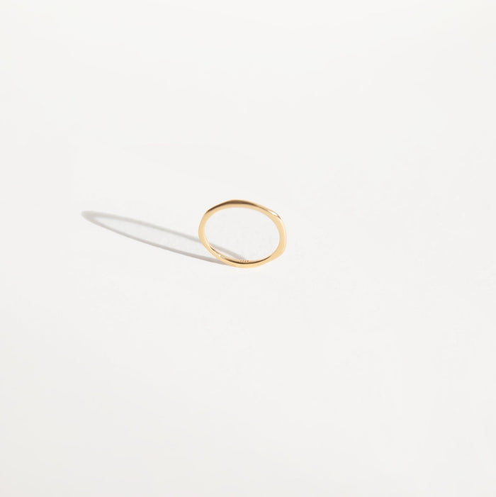 The Dune Ring by LLUME Jewelry is a simple, thin 14k gold-filled band with a subtle organic shape, shown on a white surface casting a gentle shadow—ideal for stacking or easy everyday wear.