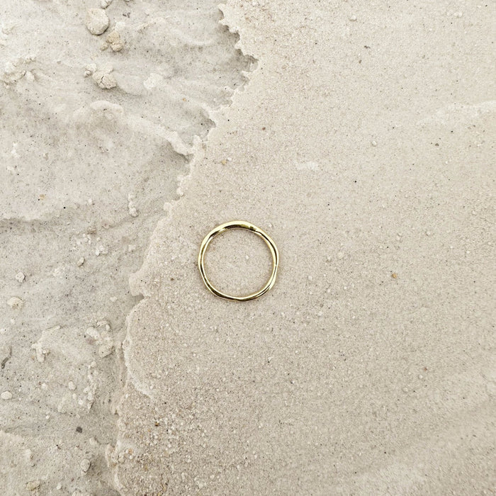 The Dune Ring by LLUME Jewelry, crafted in 14k gold-filled metal, rests on light sand where wet and dry textures meet—a versatile piece ideal for daily wear or stacking with your favorite rings.