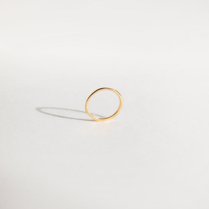 The Dune Ring by LLUME Jewelry is a simple, thin 14k gold-filled band standing upright on a white surface, its delicate design and soft shadow emphasizing its elegance—perfect for stacking and effortless daily wear.
