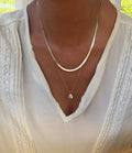 Adorned in a white blouse with lace accents, a person elegantly showcases the LLUME Jewelry Elara Classics Set—featuring two gold necklaces, including a skinny Hailey chain and a solitaire teardrop pendant—demonstrating the art of thoughtfully layered jewelry.