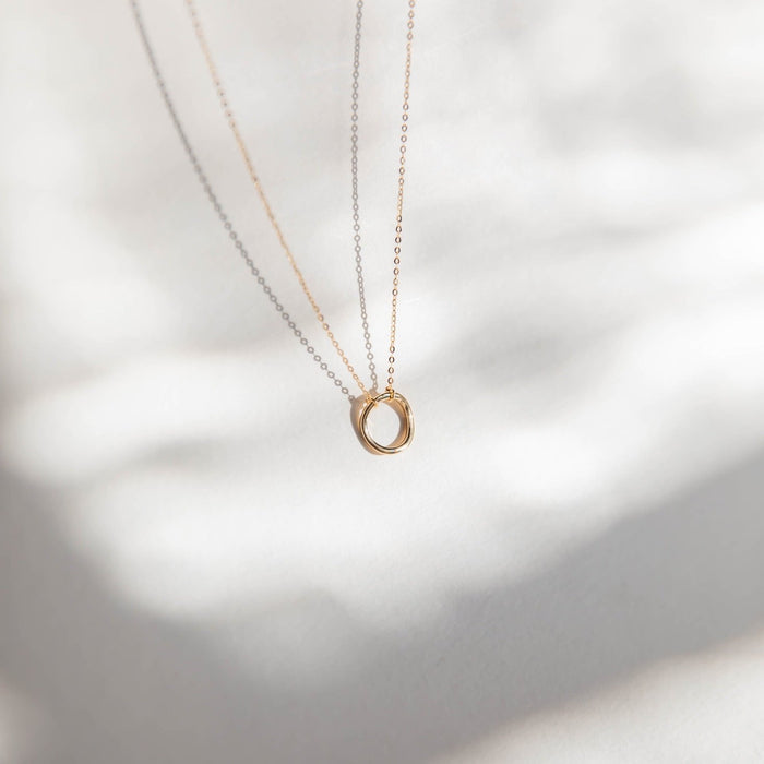 The Everything, In Time Necklace by LLUME Jewelry features two fine chain necklaces—one gold and one silver—with organic circle pendants, elegantly displayed on a softly blurred background with gentle shadows.