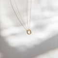 The Everything, In Time Necklace by LLUME Jewelry features two fine chain necklaces—one gold and one silver—with organic circle pendants, elegantly displayed on a softly blurred background with gentle shadows.