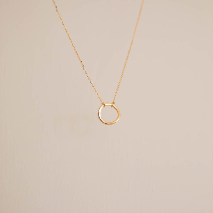 The LLUME Jewelry Everything, In Time Necklace—a delicate gold chain with a small organic circle pendant—is shown against a plain, light background.