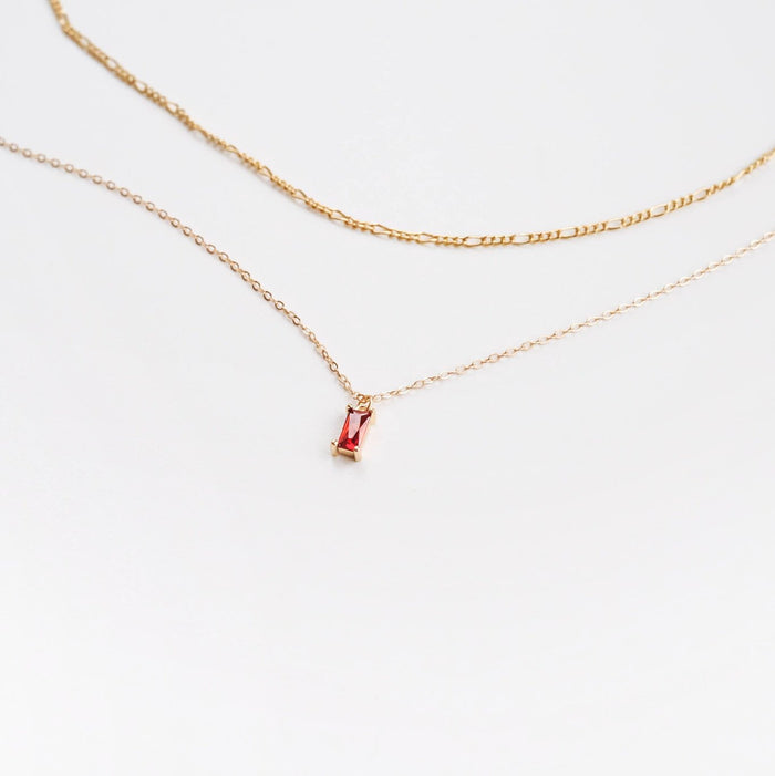 Two delicate gold necklaces from LLUME Jewelry on a white background: one is the minimalist Colette Necklace, and the other, Fate Daily, features a small rectangular red gemstone pendant.