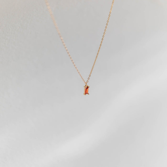 The Fate Necklace by LLUME Jewelry is a gold-plated sterling silver chain with a small rectangular orange gemstone pendant, shown on a soft light gray background.