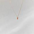 The Fate Necklace by LLUME Jewelry is a gold-plated sterling silver chain with a small rectangular orange gemstone pendant, shown on a soft light gray background.