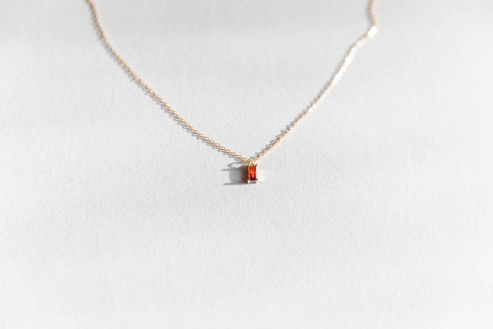 The Fate Necklace by LLUME Jewelry is a delicate gold-plated sterling silver chain with a small rectangular orange gemstone pendant, shown on a light gray background.