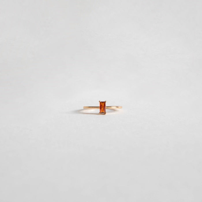 The Fate Ring by LLUME Jewelry features a delicate 14k gold-filled band with a rectangular red stone, showcased on a plain, light gray background.