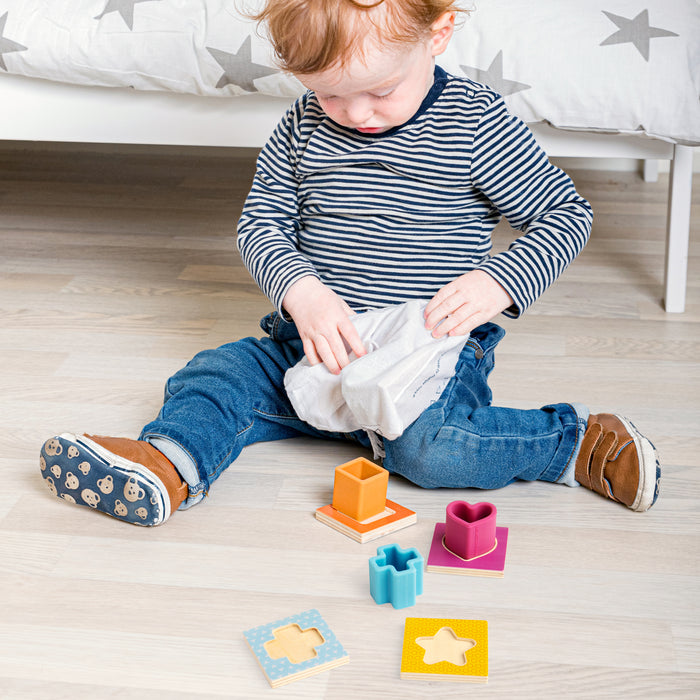 Child playing with colorful wooden shapes on a wooden floor.
