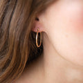 Close-up of LLUME Jewelry's Fireside Hoops, elegant 18k gold plated earrings, worn with long brown hair partially visible in soft natural light.
