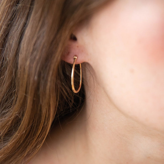 Close-up of LLUME Jewelry's Fireside Hoops, elegant 18k gold plated earrings, worn with long brown hair partially visible in soft natural light.