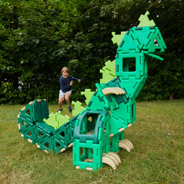 Child playing with a large green dinosaur toy in a grassy area