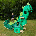 Child playing with a large green dinosaur toy in a grassy area