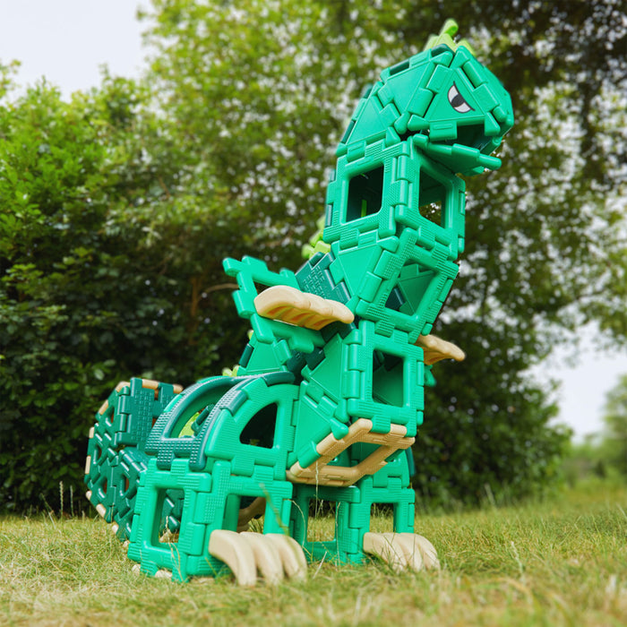 Green dinosaur toy made of interlocking bricks on grass with trees in the background