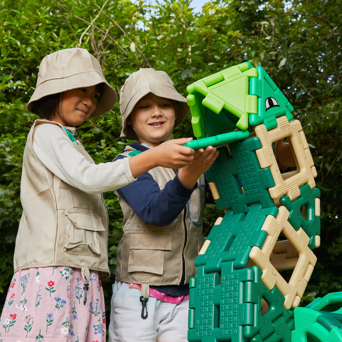 Two children playing with a green toy dinosaur outdoors.