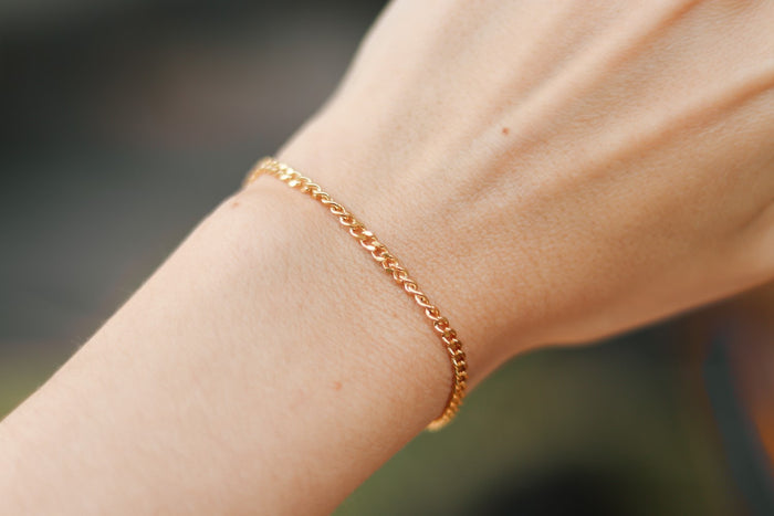 A gold tone stainless steel chain bracelet being worn on a person's wrist.