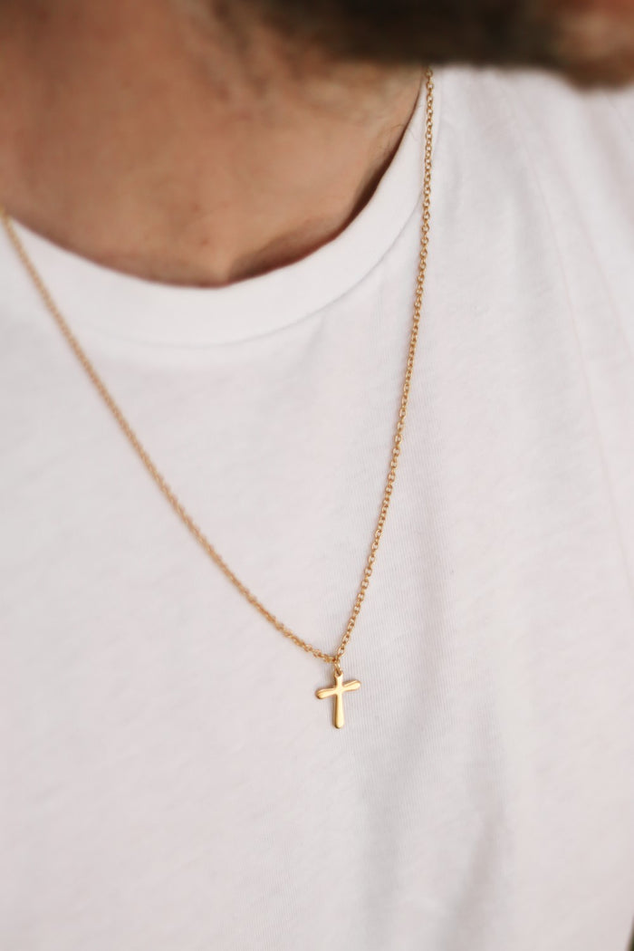 A gold-tone stainless steel cross necklace with a chain and clasp closure, worn by a man.