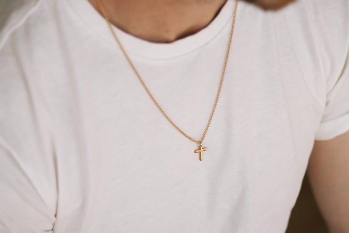 Gold cross chain necklace for men on a white shirt with a plain background
