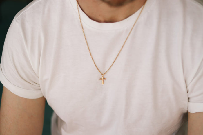 Gold cross chain necklace for men on a white shirt with a plain background