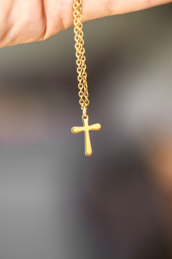 Gold cross chain necklace for men on a white shirt with a plain background