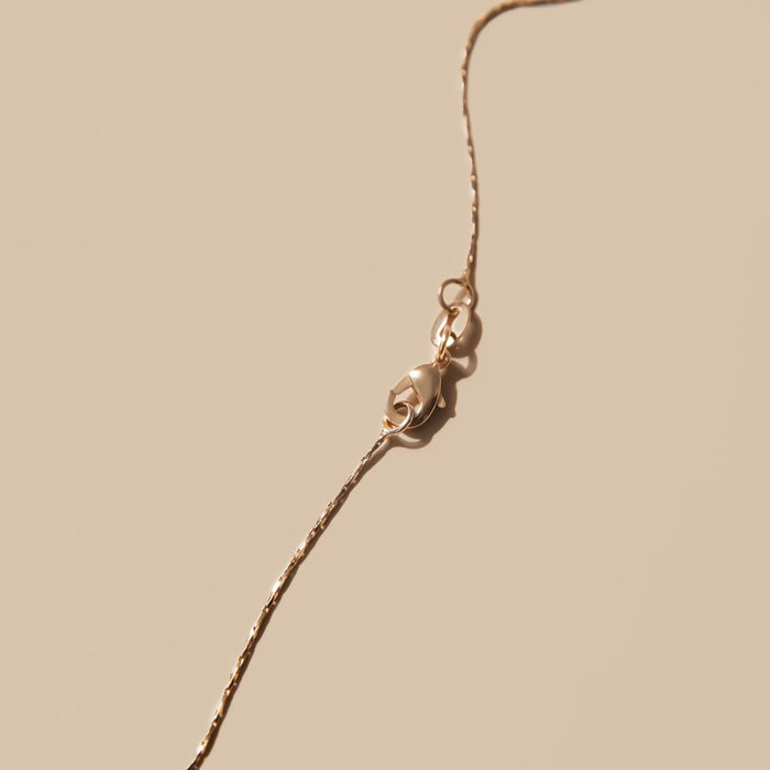 Close-up of the Golden Hour Chain by LLUME Jewelry, a delicate 18k gold-filled necklace with a lobster clasp, displayed on a soft beige background.