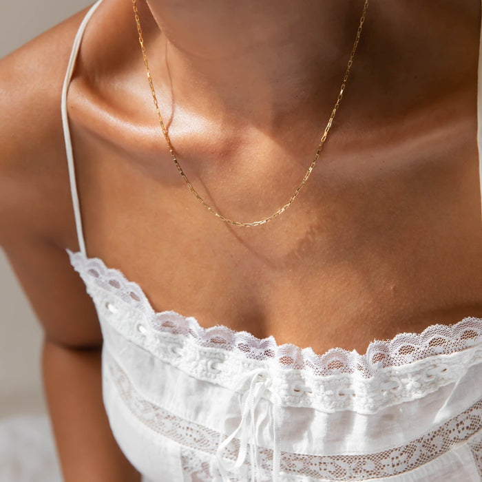 A person wears the LLUME Jewelry Harlow Chain necklace in 18k gold fill and a white lace-trimmed camisole top, highlighting their neck, collarbone, and upper chest.