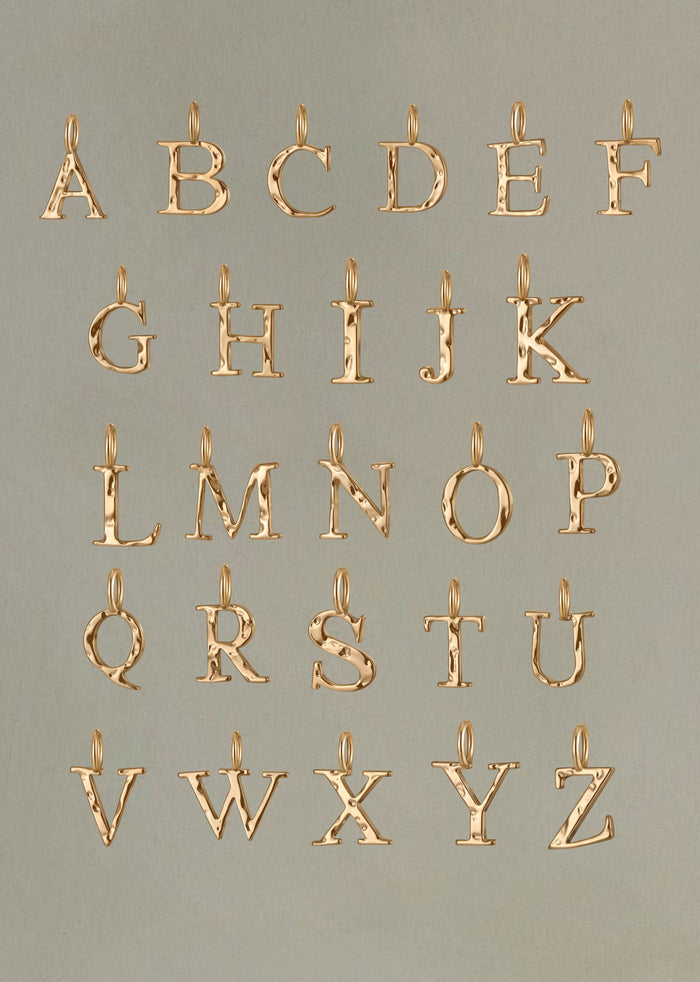 LLUME Jewelry's Initial Necklace Set displays gold alphabet charms A-Z in four rows on a neutral background, each with a top loop—ideal for creating personalized necklaces or layering with other chains.