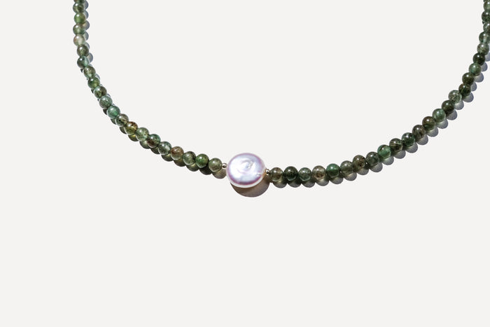 The Isla Necklace by LLUME Jewelry features handcrafted small round green natural stones and a central larger white pearl, shown on a white background.