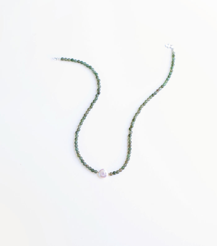 The Isla Necklace by LLUME Jewelry showcases handcrafted design with small green natural stones and a central round white pearl, presented on a plain white background.