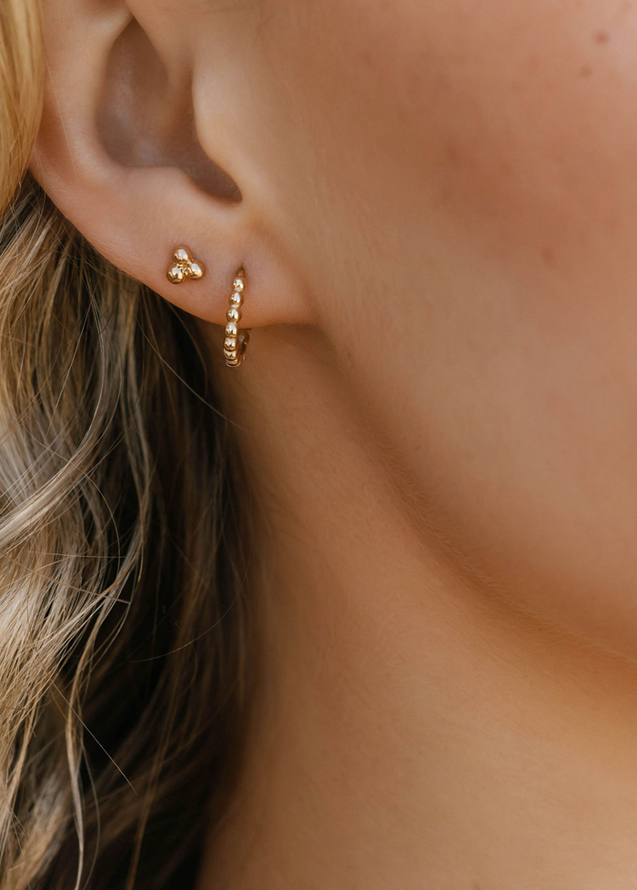 Close-up of a woman's ear wearing the LLUME Jewelry June-Prosecco Set, featuring a gold cluster stud and a textured beaded hoop. Blonde hair is partly visible on the left.
