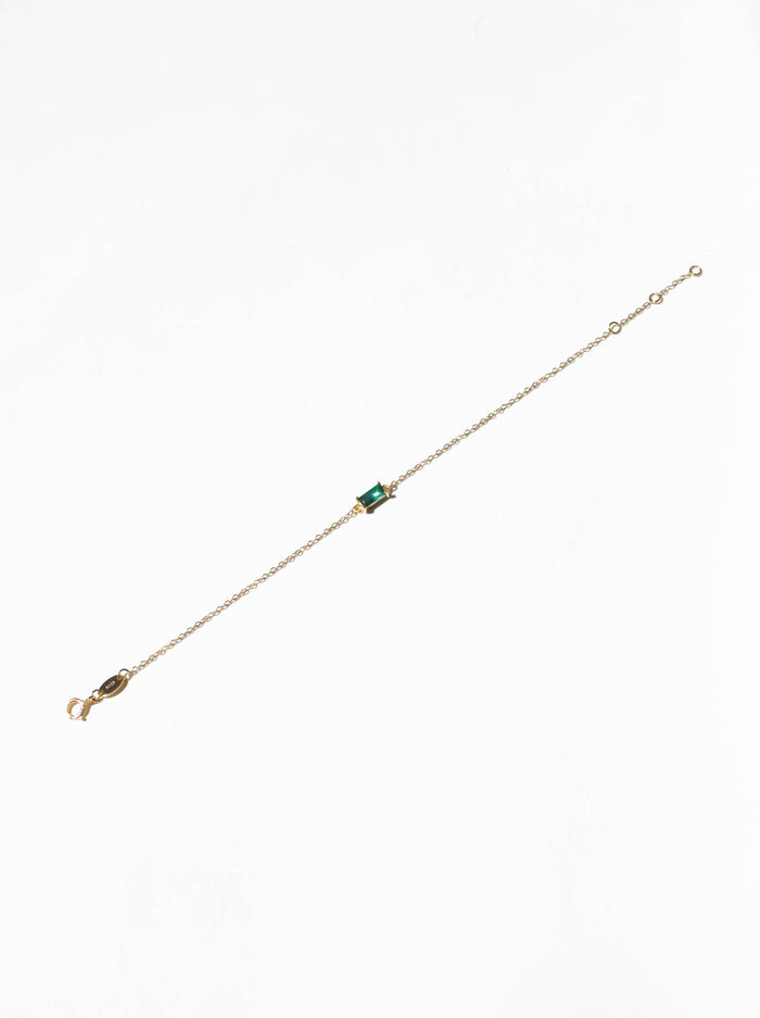The Kismet Bracelet by LLUME Jewelry is a gold-plated, adjustable piece with a small emerald green rectangular gemstone at the center, perfect for adding a subtle pop of color to your look. Displayed on a white background.