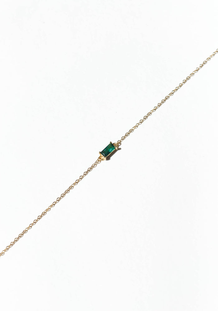 The Kismet Bracelet by LLUME Jewelry features a gold-plated chain with a central rectangular emerald-green gemstone. Adjustable for comfort, this dainty accessory brings elegant charm to any outfit and is displayed on a plain white background.