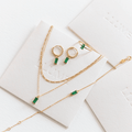 Effortless layering shines in the Kismet Capsule set by LLUME Jewelry—gold pieces with green rectangular gemstones (necklace, bracelet, ring, earrings), elegantly displayed on white cards with subtle embossed branding.