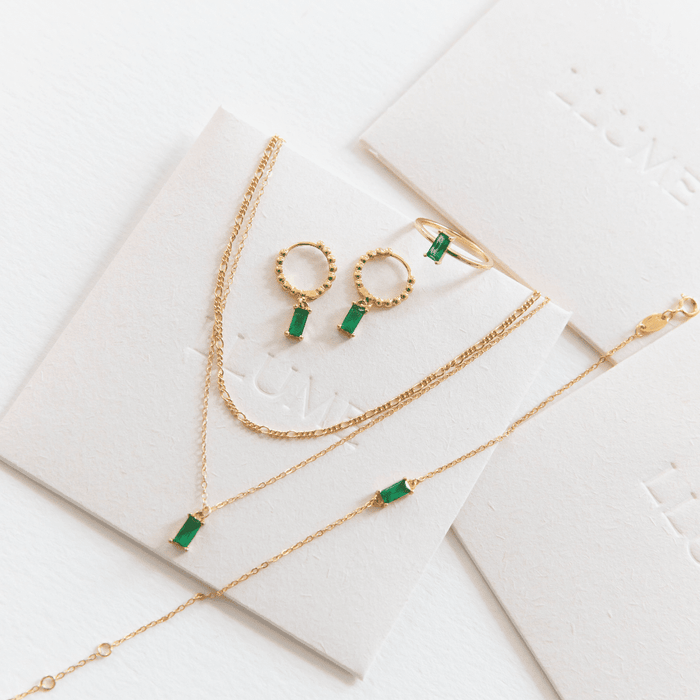 Effortless layering shines in the Kismet Capsule set by LLUME Jewelry—gold pieces with green rectangular gemstones (necklace, bracelet, ring, earrings), elegantly displayed on white cards with subtle embossed branding.