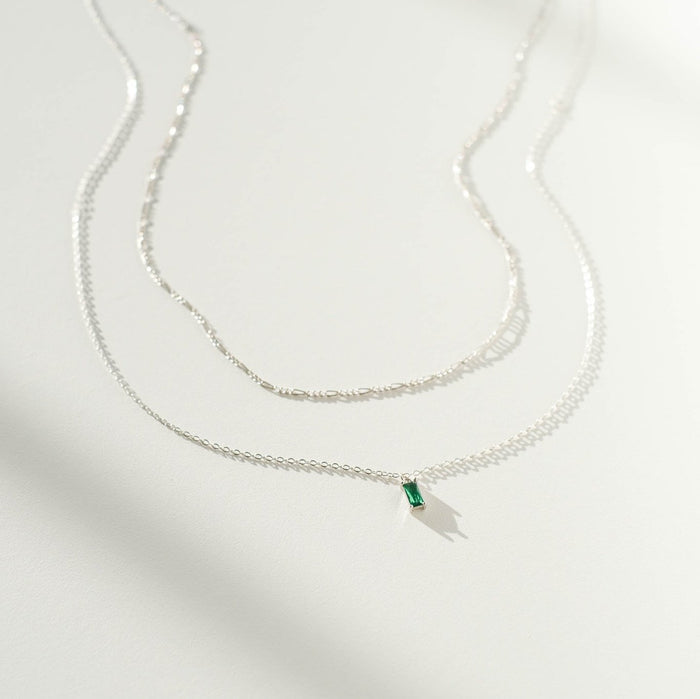 Two delicate silver necklaces from LLUME Jewelry’s Kismet Daily Set Silver are displayed on a white surface, casting soft shadows in the light.