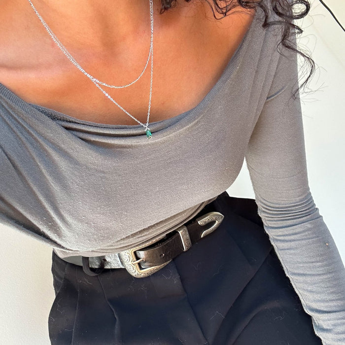 A person wearing a grey off-the-shoulder long-sleeve top, black high-waisted pants with a silver-buckled belt, and the Kismet Daily Set Silver by LLUME Jewelry.