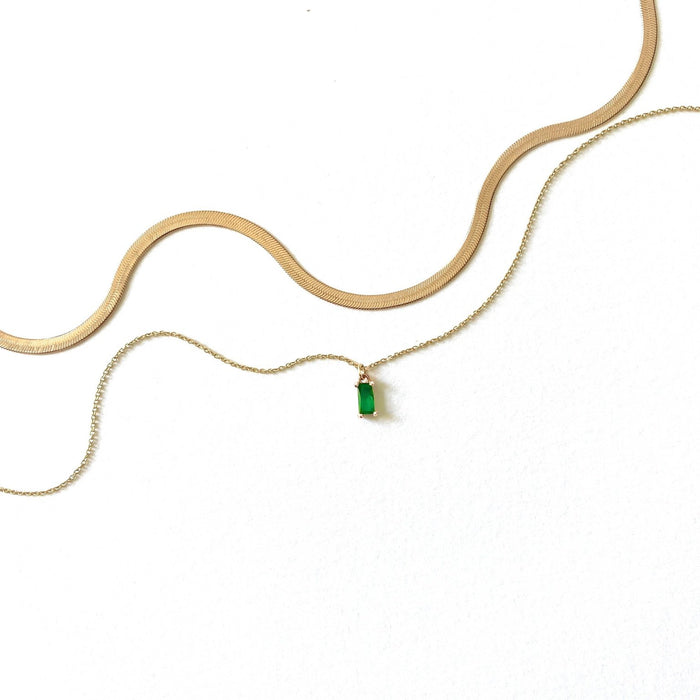 The Kismet Hailey Set features two gold necklaces on a white background: a herringbone Skinny Hailey chain and the emerald green Kismet Necklace with a delicate chain and rectangular green pendant.