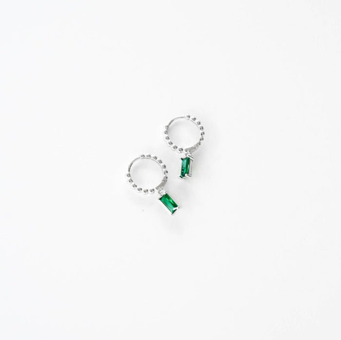 The Kismet Hoops Silver by LLUME Jewelry are dainty charm earrings with silver hoops, small clear stones, and a rectangular emerald green gemstone, shown on a white background.
