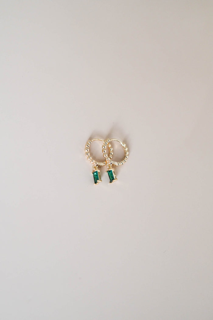 The Kismet Hoops by LLUME Jewelry are gold plated earrings with small beaded details and rectangular green gemstone charms, shown on a plain light background.