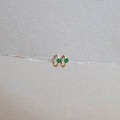The Kismet Huggies by LLUME Jewelry are gold-plated green earrings with stone accents, shown on torn white paper against a minimalist, neutral backdrop.