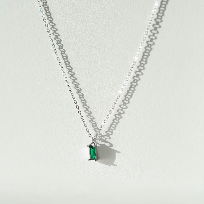 The Kismet Necklace Silver by LLUME Jewelry features a thin sterling silver chain and a rectangular green gemstone pendant, ideal for dainty jewelry lovers. It creates a soft shadow on a light background.