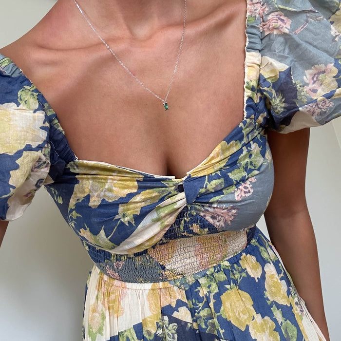 A person in a blue, yellow, and white floral dress with puffed sleeves wears dainty jewelry—a LLUME Jewelry Kismet Necklace Silver. The image is cropped at the neck and waist.