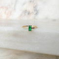 The Kismet Ring by LLUME Jewelry features a rectangular emerald green stone set in a 14k gold-filled band, displayed on white marble with soft natural light.