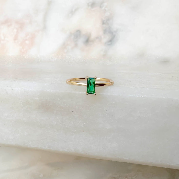 The Kismet Ring by LLUME Jewelry features a rectangular emerald green stone set in a 14k gold-filled band, displayed on white marble with soft natural light.