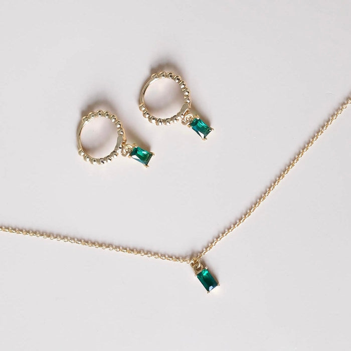 The Kismet Set by LLUME Jewelry features a gold necklace and matching earrings, each with a petite rectangular emerald pendant, elegantly displayed on a plain white background.